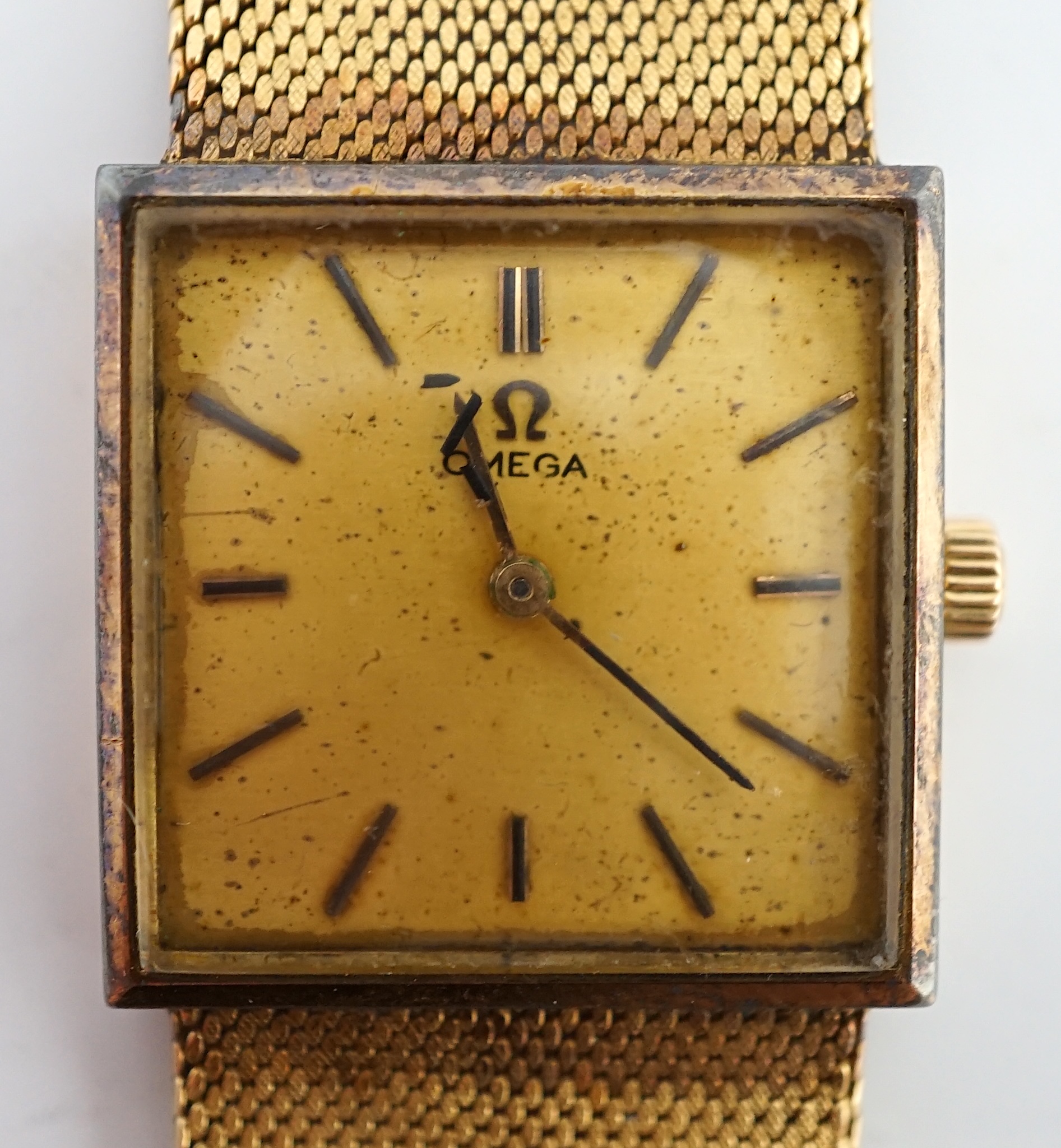 A gentleman's 18k gold Omega dress wrist watch, the square dial with baton markers, on integral textured close-link flexible Omega bracelet with clasp